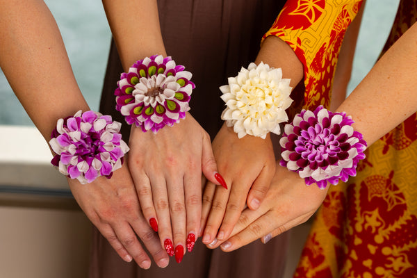 Collection of colorful floral orchid wristlets worn on four hands, showcasing a variety of vibrant designs.