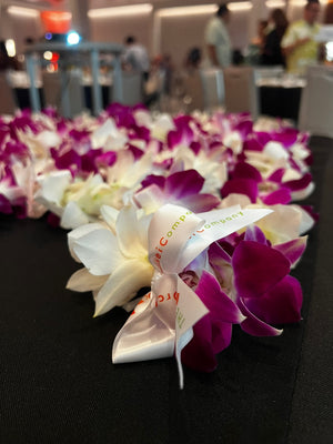 Single purple and white orchid leis laid out on a table next to an Orchid Lei Company ribbon.