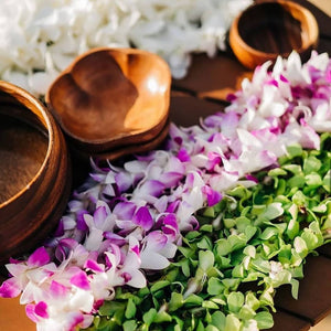 Three empty wooden bowl stacks placed on a wooden table, surrounded by single strand orchid leis in shades of white, purple, and green.