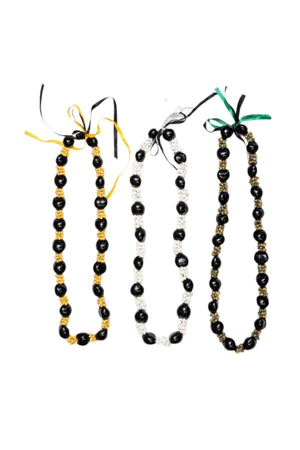 Collection of three leis featuring alternating patterns of glossy black Kukui nuts and Mongo shells in natural yellow, white, and green tones, tied with yellow, black, and green ribbons.