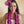 Woman sitting on a couch wearing a purple floral headpiece and a fluffy purple orchid lei.