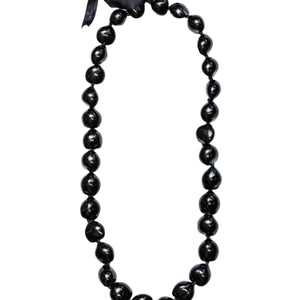 A black kukui nut lei with a smooth, glossy finish, tied together with a black ribbon.