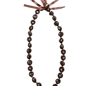 A brown kukui nut lei with a smooth, glossy finish, tied together at the top with a brown ribbon. 