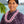 Man wearing a purple patterned shirt and a pink and purple orchid spiral lei, with Diamond Head, a palm tree, and the ocean in the background.