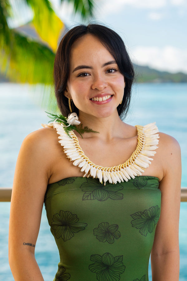 A woman wearing a green dress and a traditional micro ginger lei, ideal for weddings, with a background of a tropical setting.