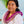 Young girl wearing a white dress and a purple and white orchid lei with white petals overlapping the purple, standing with Diamond Head, a palm tree, and the ocean in the background.