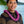 Man wearing a black and brown patterned shirt and a unique deluxe round purple orchid lei, with Diamond Head, a palm tree, and the ocean in the background.