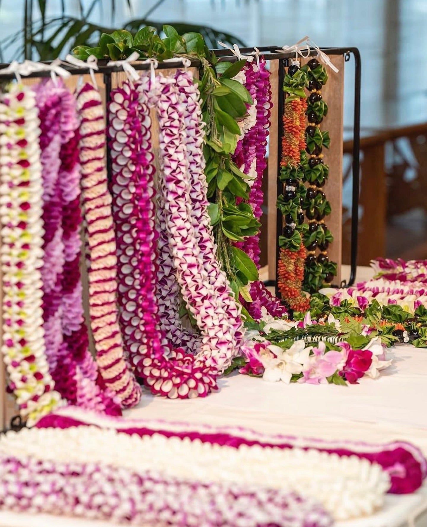 Display table featuring a variety of orchid leis laid out on the table and hanging above, showcasing different colors, designs, and styles.