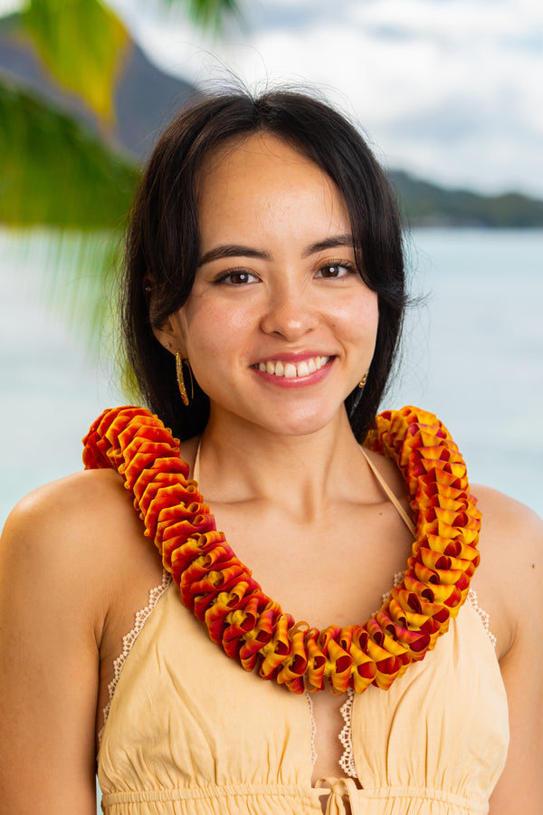 Girl in her 20s wearing a light yellow dress and a bright red-orange orchid lei, with Diamond Head, a palm tree, and the ocean in the background.
