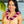A woman wearing a light yellow dress and a two-shaded purple spiral orchid lei, standing with Diamond Head, a palm tree, and the ocean in the background.