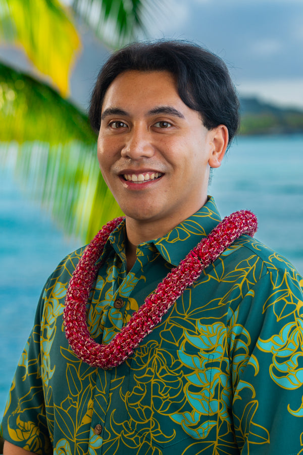 Man wearing a pure red cigar flower lei with Diamond Head, a palm tree, and the ocean in the background.
