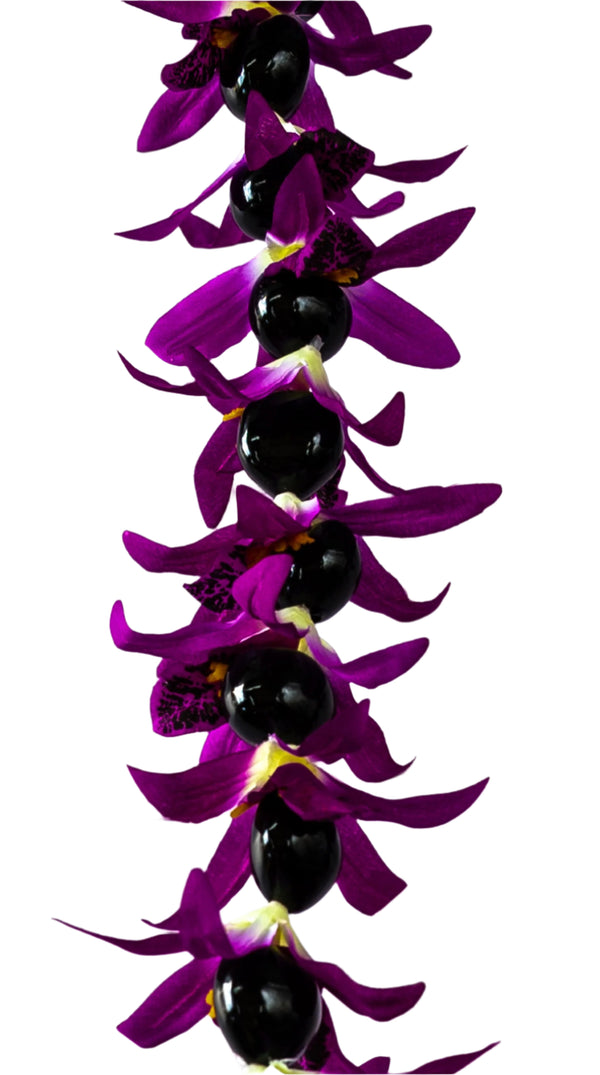 Close-up of a lei featuring vibrant silk fuchsia orchids and glossy black kukui nuts, set against a white background.