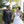 Elderly wedding couple wearing single-strand orchid leis in purple and green, standing together with a tropical background of palm trees and lush greenery.