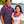A man and woman standing side by side, each wearing a classic single purple orchid lei, with Diamond Head, a palm tree, and the ocean in the background.