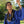 Graduate in blue cap and gown celebrating outdoors with mongo shell, kukui, and single ti leaf leis.
