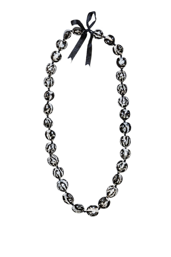 A lei made of polished black and white kukui nuts with a smooth, glossy finish, featuring a black ribbon tie at the top.