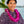 A man wearing a two-tone purple patterned shirt and a fluffy purple orchid lei in front of Diamond Head, with a palm tree and the ocean in the background.
