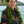 Man wearing a fresh and lush green ti leaf maile lei with Diamond Head, a palm tree, and the ocean in the background.