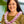 Woman wearing a green leaf design top and a textured purple spiral orchid lei, with Diamond Head, a palm tree, and the ocean in the background.